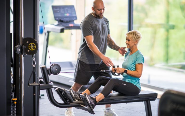 Mann hilft Frau beim Training an einer Fitnessmaschine in einem modernen Fitnessstudio.